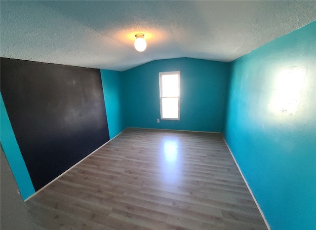 spare room featuring a textured ceiling, hardwood / wood-style flooring, and lofted ceiling