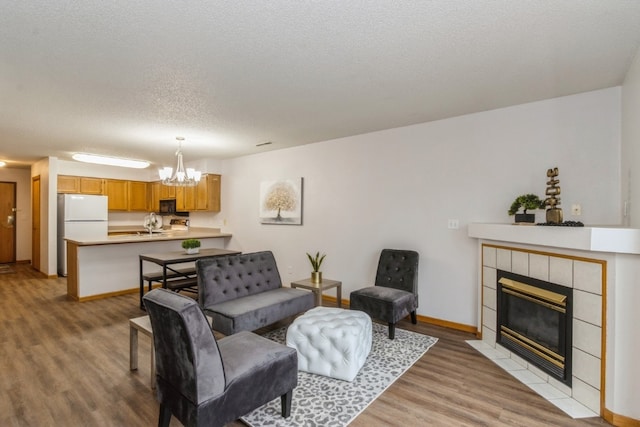 living room featuring an inviting chandelier, sink, light wood-type flooring, a textured ceiling, and a tiled fireplace