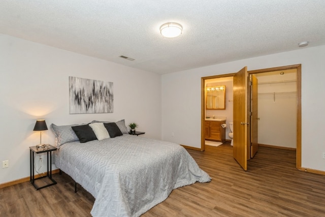 bedroom featuring ensuite bath, a spacious closet, a textured ceiling, and hardwood / wood-style flooring