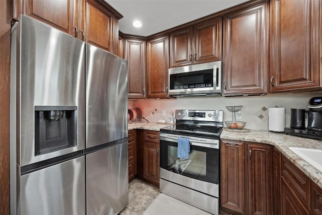 kitchen featuring light stone counters, decorative backsplash, light tile patterned flooring, and appliances with stainless steel finishes