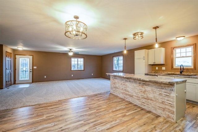 kitchen with pendant lighting, light wood-type flooring, white cabinetry, and sink