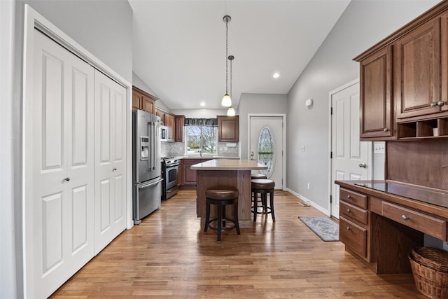 kitchen featuring hanging light fixtures, light hardwood / wood-style flooring, vaulted ceiling, a kitchen island, and appliances with stainless steel finishes