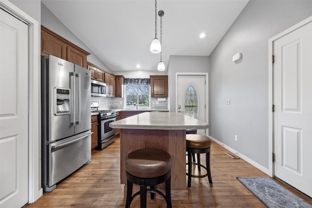 kitchen with hardwood / wood-style flooring, a kitchen island, appliances with stainless steel finishes, and vaulted ceiling