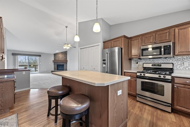 kitchen featuring stainless steel appliances, ceiling fan, light hardwood / wood-style flooring, a center island, and a stone fireplace