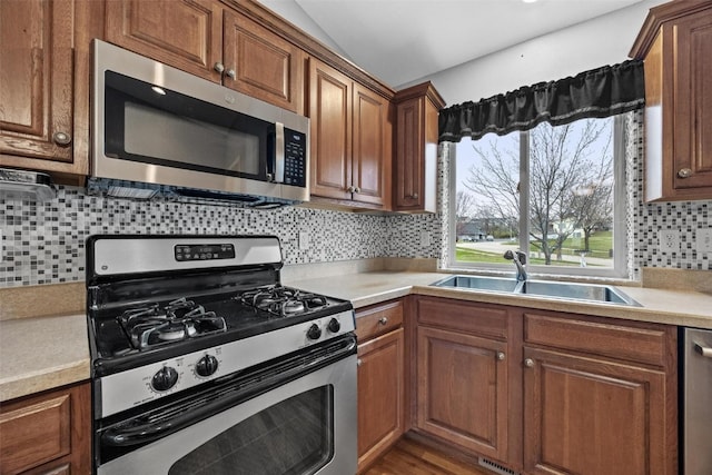 kitchen with appliances with stainless steel finishes, backsplash, vaulted ceiling, sink, and wood-type flooring