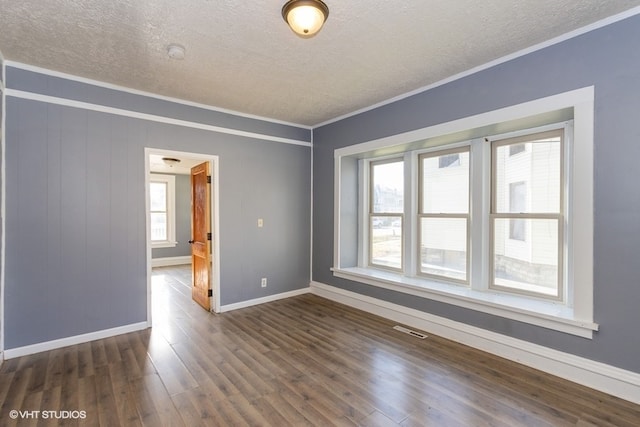 empty room with a textured ceiling, crown molding, and dark wood-type flooring