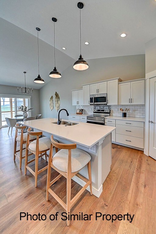 kitchen with a kitchen island with sink, white cabinets, stainless steel appliances, and light hardwood / wood-style floors