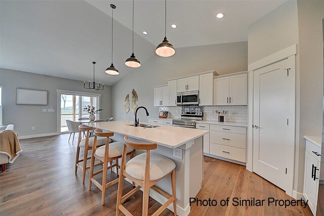 kitchen with a center island with sink, sink, appliances with stainless steel finishes, white cabinetry, and a breakfast bar area