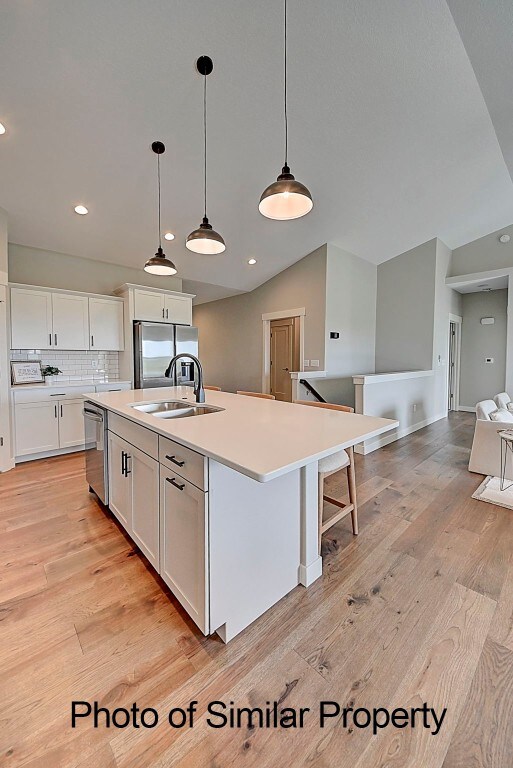 kitchen with a center island with sink, white cabinets, sink, light hardwood / wood-style flooring, and stainless steel appliances