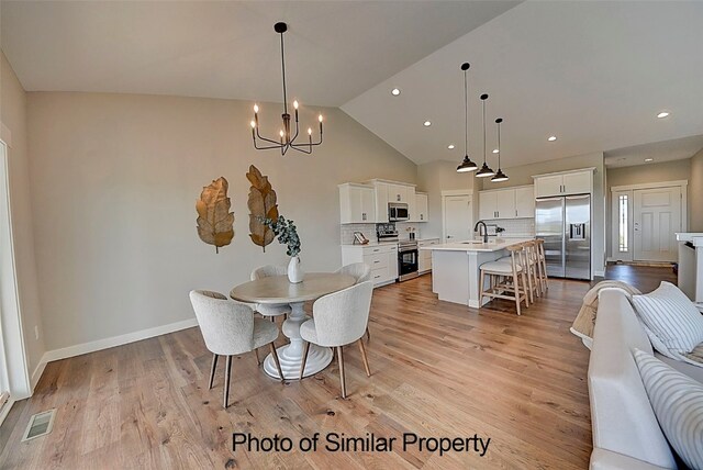 dining room with a chandelier, light wood-type flooring, vaulted ceiling, and sink