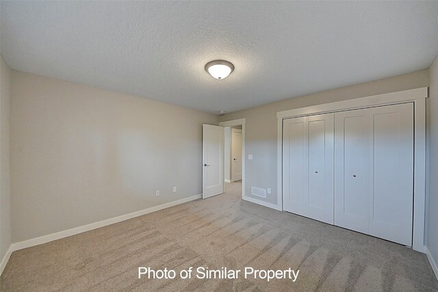 unfurnished bedroom featuring a textured ceiling, light colored carpet, and a closet