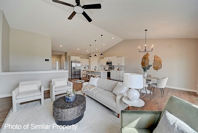 living room with light hardwood / wood-style flooring, ceiling fan with notable chandelier, vaulted ceiling, and sink