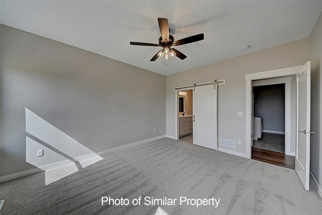 unfurnished bedroom with light carpet, a barn door, ensuite bath, and ceiling fan