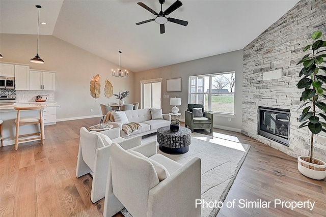 living room featuring ceiling fan with notable chandelier, a stone fireplace, lofted ceiling, and light hardwood / wood-style flooring