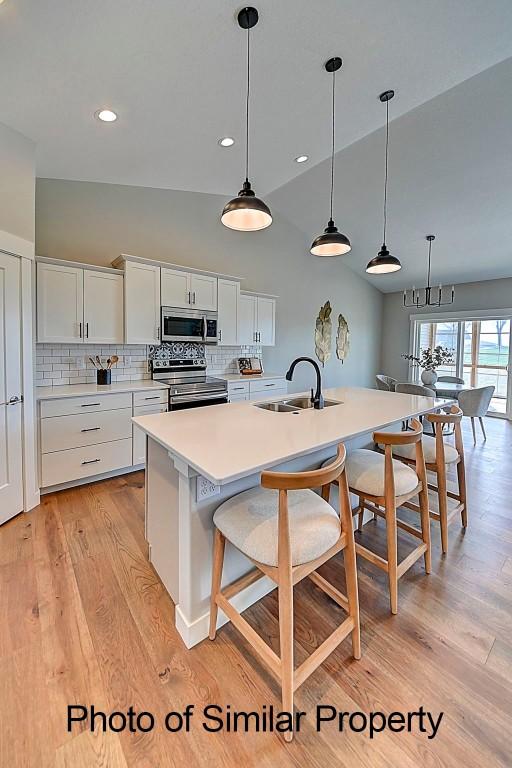 2933 Clubhouse Dr, Marion, IA 52302 - kitchen featuring stainless steel appliances, a kitchen breakfast bar, decorative backsplash, light wood-style flooring, and white cabinets