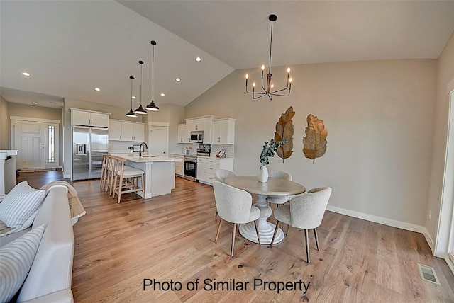 dining room featuring light hardwood / wood-style floors, sink, high vaulted ceiling, and an inviting chandelier