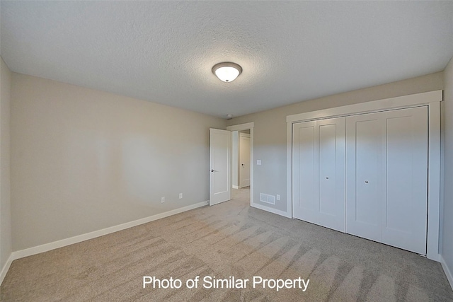 unfurnished bedroom with a textured ceiling, light carpet, and a closet