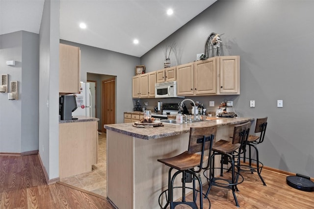 kitchen featuring kitchen peninsula, a kitchen breakfast bar, light brown cabinetry, light hardwood / wood-style flooring, and lofted ceiling