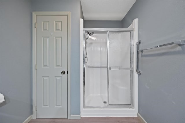 bathroom with a textured ceiling, wood-type flooring, and an enclosed shower