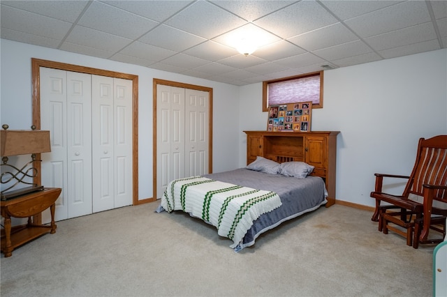 carpeted bedroom with a paneled ceiling and multiple closets