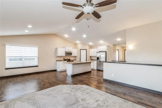 kitchen featuring vaulted ceiling, an island with sink, white cabinets, light stone counters, and stainless steel appliances