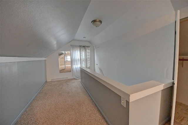 hallway with a textured ceiling, light colored carpet, and lofted ceiling