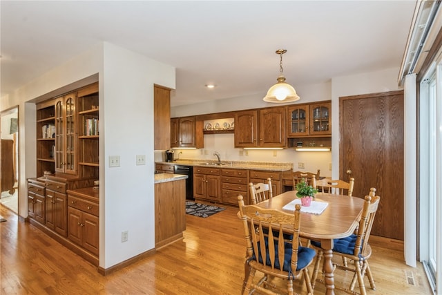 kitchen featuring sink, hanging light fixtures, light hardwood / wood-style flooring, light stone countertops, and black dishwasher