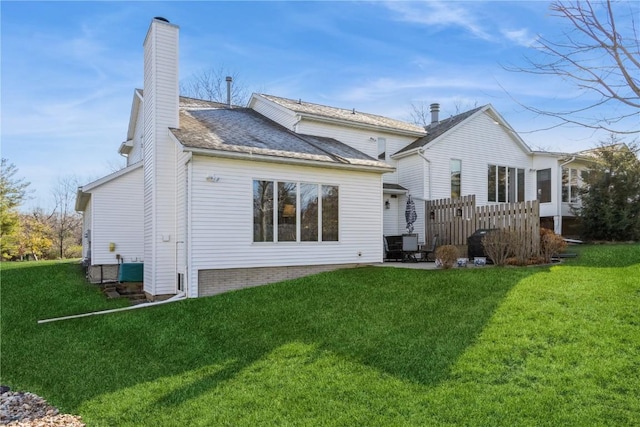 rear view of house with a chimney, a patio area, and a lawn