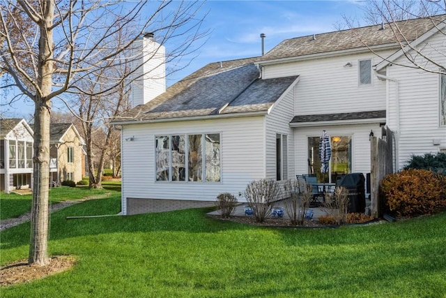 rear view of house featuring a lawn, roof with shingles, a chimney, and a patio