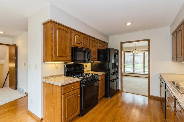 kitchen with visible vents, black appliances, light wood finished floors, and a sink