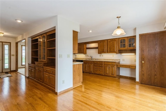 kitchen featuring open shelves, glass insert cabinets, a sink, light wood-style floors, and brown cabinetry