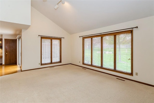 empty room featuring high vaulted ceiling, rail lighting, visible vents, light carpet, and baseboards