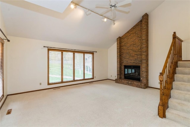 unfurnished living room with a brick fireplace, stairs, track lighting, carpet, and lofted ceiling