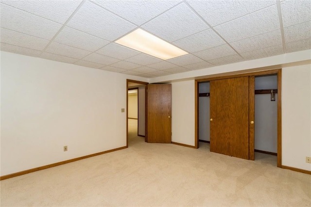unfurnished bedroom featuring baseboards, light carpet, and a drop ceiling