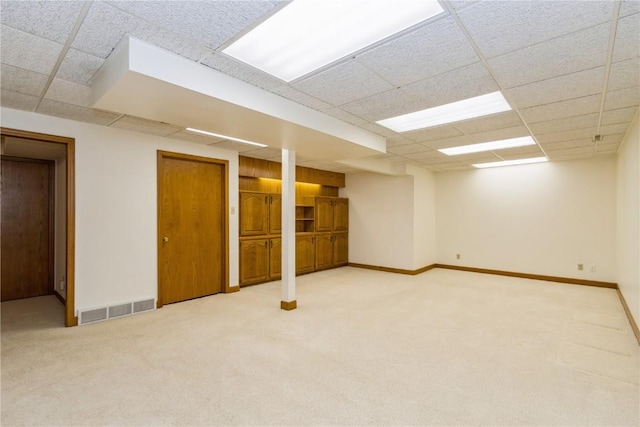 finished below grade area featuring a paneled ceiling, visible vents, light carpet, and baseboards