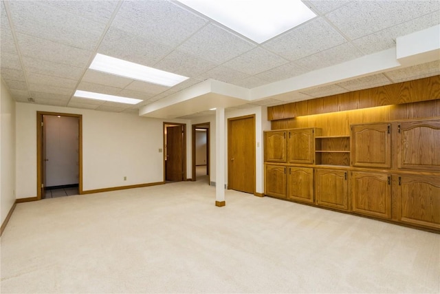finished basement featuring a paneled ceiling, light carpet, and baseboards