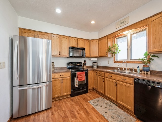 kitchen featuring black appliances, light wood-type flooring, sink, and a textured ceiling