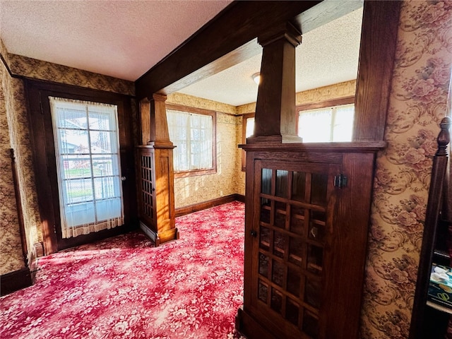 hallway with a textured ceiling, ornate columns, and plenty of natural light