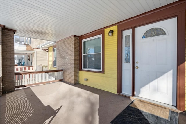 entrance to property featuring a porch and brick siding