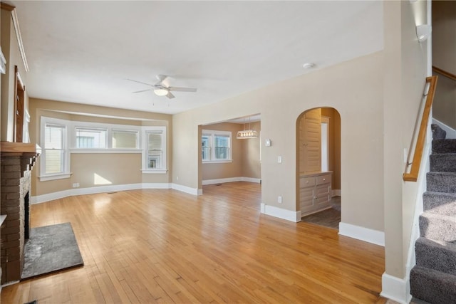 living area featuring ceiling fan, arched walkways, a fireplace, light wood-style floors, and stairway