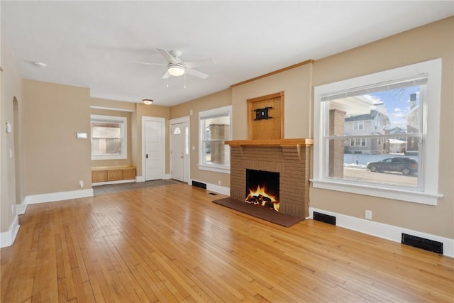 unfurnished living room featuring a brick fireplace, light wood-style flooring, visible vents, and arched walkways