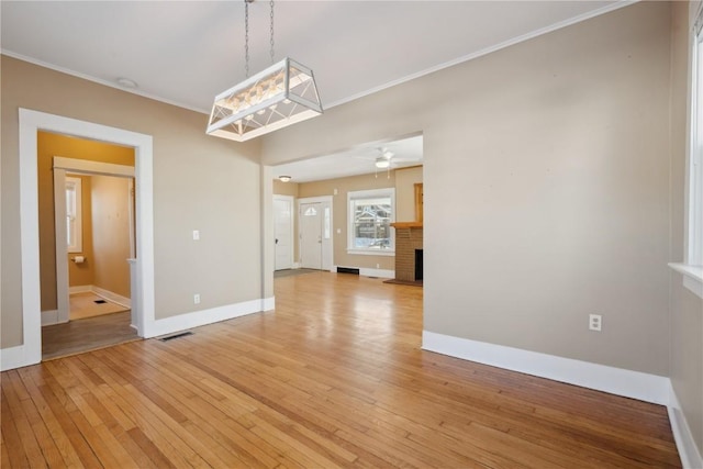 unfurnished dining area featuring light wood-style flooring, visible vents, baseboards, a brick fireplace, and crown molding