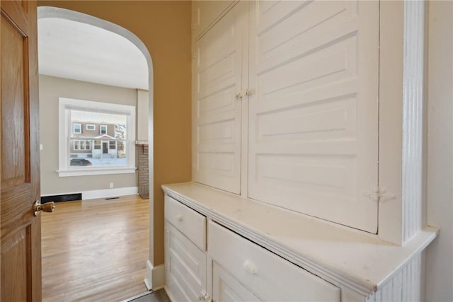 interior space featuring arched walkways, light wood-style flooring, and baseboards