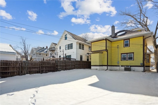 snow covered rear of property with a chimney, cooling unit, fence, and a residential view