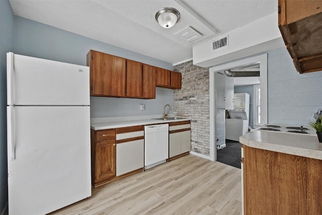 kitchen with white appliances, sink, a textured ceiling, light hardwood / wood-style floors, and brick wall