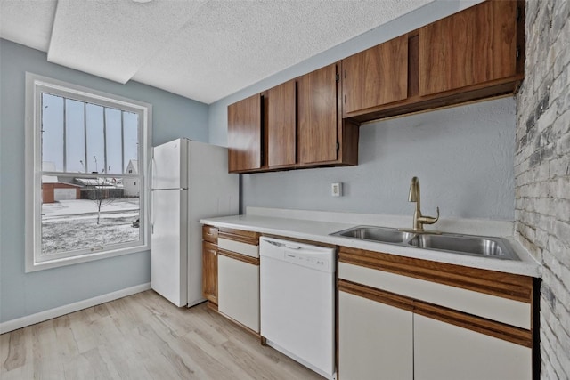 kitchen with light wood-type flooring, a textured ceiling, white appliances, and sink