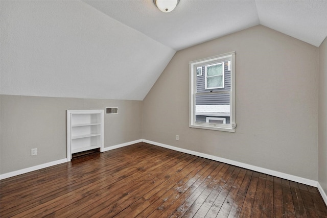 additional living space featuring built in features, a textured ceiling, vaulted ceiling, and dark wood-type flooring