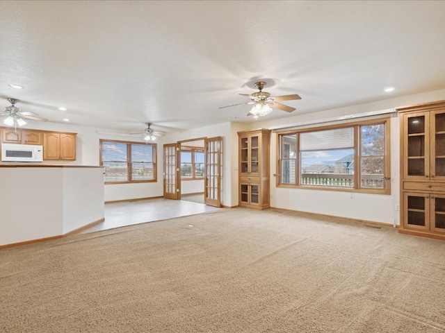 unfurnished living room with light carpet, french doors, ceiling fan, and a textured ceiling