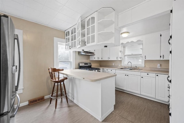 kitchen with hardwood / wood-style floors, white cabinets, sink, kitchen peninsula, and stainless steel appliances