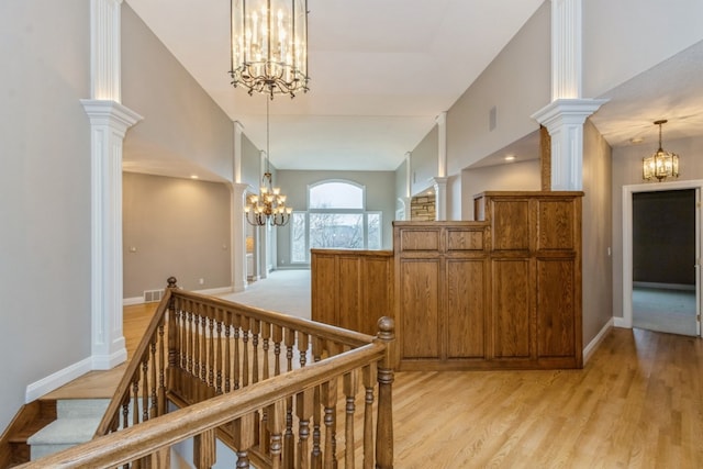 hall with light wood-type flooring, an inviting chandelier, and ornate columns